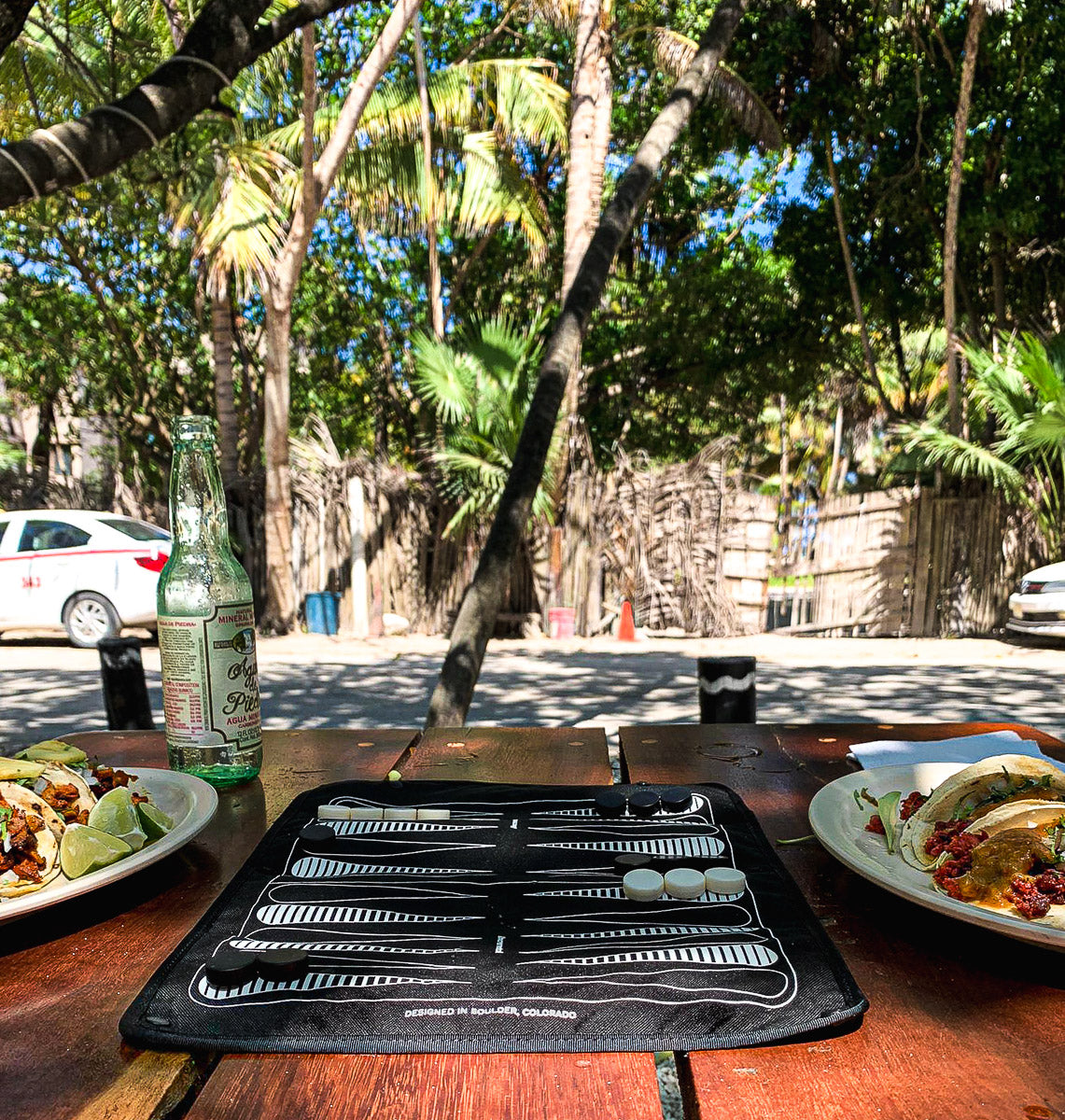 MagBoard with backgammon setup on a table in a tropical location, plates of tacos also on table